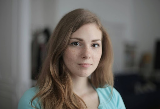 Professional headshot of a woman named Kate, smiling confidently, with long brown hair styled neatly and wearing a stylish top, set against a neutral background.