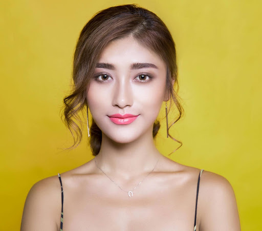 Professional headshot of a woman named Kathleen, smiling warmly, with long brown hair and wearing a black top, set against a yellow background.